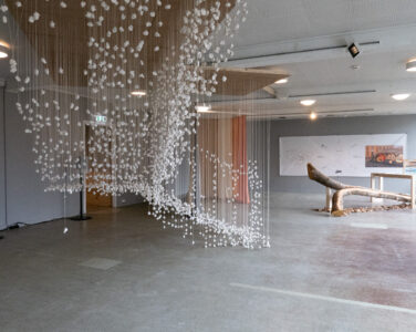 I front: «Jeg var her» (2025) av Kåre Aleksander Grundvåg og Alexander Rishaug, til venstre bak tekstil: «Fargeprismer fra naturen» (2025) av Hilde Hauan Johnsen, og til høyre bak: «Kokegamme» (2025) av Joar Nango, og fettstifttegninger av Marit Bockelie, Eystein Talleraas, Arne-Terje Sæther. (Foto: Kai Mørk Mortensen.)