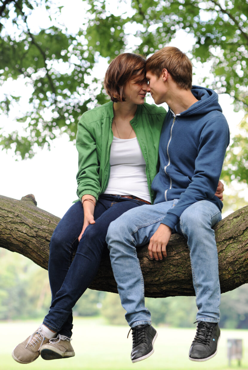 Ungt forelsket par i naturen. Sommerforelskelse. Ung kjærlighet. Forelskelse. Forelsket. Ung kvinne. Ung mann. Lykke. Nyter livet. Livsnyter. Tenåringer. Sitter i tre. Hettegenser. Dongeri. Livsglede. Young couple out in nature. (Modellklarert illustrasjonsfoto: Frank May/NTB.)