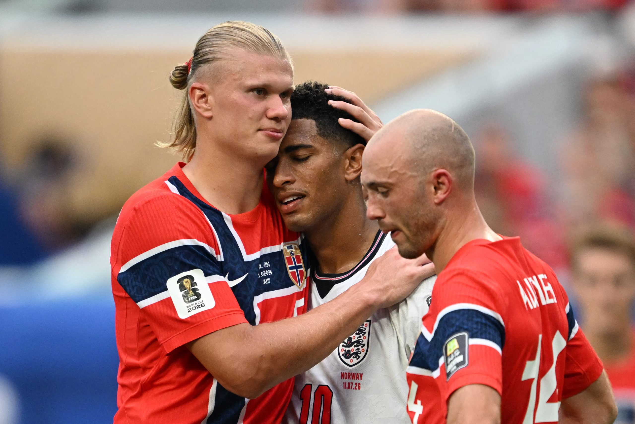 Erling Braut Haaland klemmer kameraten Jude Bellingham (England) etter kvartfinalen i VM 2026. Fredrik Aursnes (Norge) sørger stoisk i forgrunnen. (Foto: AFP.)